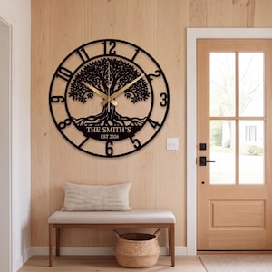 May include: A circular black wall clock featuring a detailed tree silhouette at its center. The clock face displays large black numerals and gold-colored hands. Below the tree, the text reads THE SMITH'S and EST 2026 in a clean, bold font.