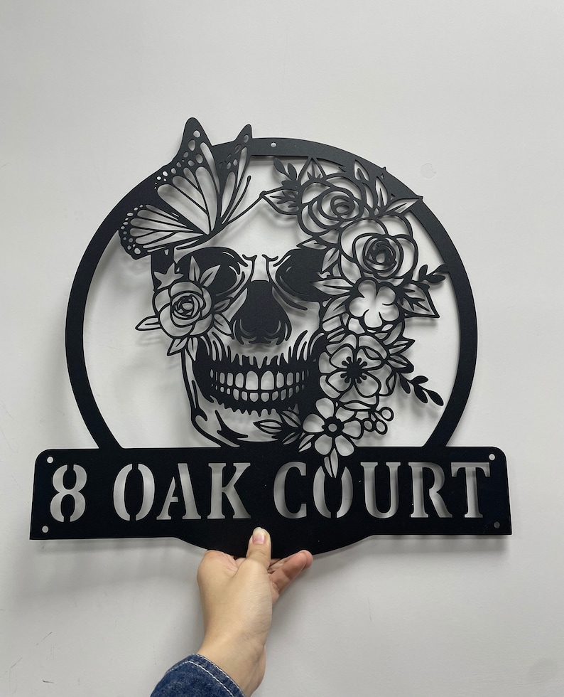May include: Black metal house number sign with a skull design surrounded by flowers and a butterfly. The sign reads "8 OAK COURT".