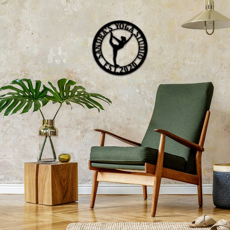 Może przedstawiać: Czarna metalowa dekoracja ścienna z sylwetką jogi i tekstem "Sandra's Yoga Studio Est. 2020".
