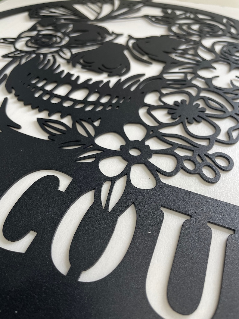 May include: Black metal wall decor featuring a skull with floral details and the word "COUT" cut out.