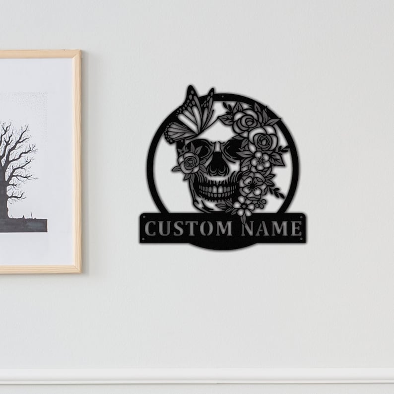 May include: Black metal wall art featuring a skull with flowers and a butterfly. The skull is surrounded by a circle and the text "CUSTOM NAME" is below the circle.