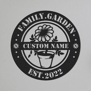 May include: Black and white metal sign with the text "FAMILY.GARDEN" in a circle around a stylized flower in a pot. The text "CUSTOM NAME" is in a banner below the flower and the text "EST. 2022" is below the banner.