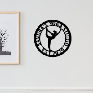 Może przedstawiać: Czarny metalowy znak z sylwetką jogi i tekstem "Sandra's Yoga Studio Est. 2020".