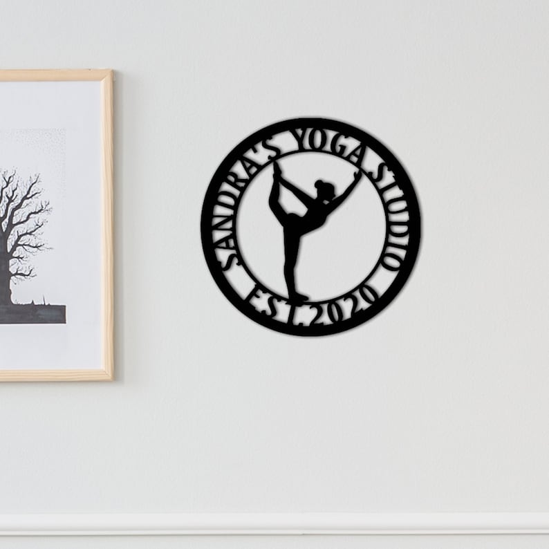 Może przedstawiać: Czarny metalowy znak z sylwetką jogi i tekstem "Sandra's Yoga Studio Est. 2020".