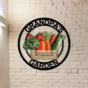 May include: Black metal sign with the words "Grandpa's Garden" in a circular design. The sign features a wooden crate filled with colorful vegetables, including tomatoes, carrots, and squash.
