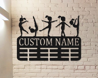May include: Black metal wall-mounted medal display with a personalized nameplate and silhouettes of gymnasts. The display has 10 rows of medal hooks.