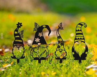 May include: Four black metal garden gnomes with whimsical designs. Each gnome has a different hat and facial expression. The gnomes are standing in a grassy area with fall leaves.