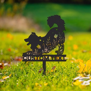 May include: Black metal garden stake with a dog silhouette and floral cutouts. The dog is in a playful pose, with the text "CUSTOM TEXT" below. The stake is in a grassy area with fallen leaves.