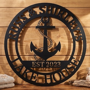 May include: A circular black metal wall sign featuring a central anchor graphic wrapped in rope. The text RUSS & SHIRLEY'S is arched along the top, and LAKE HOUSE is arched along the bottom. The centre includes the text EST 2023 in a straight line.