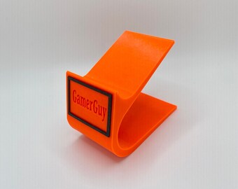 May include: Orange plastic phone stand with a black rectangular label that says "GamerGuy".