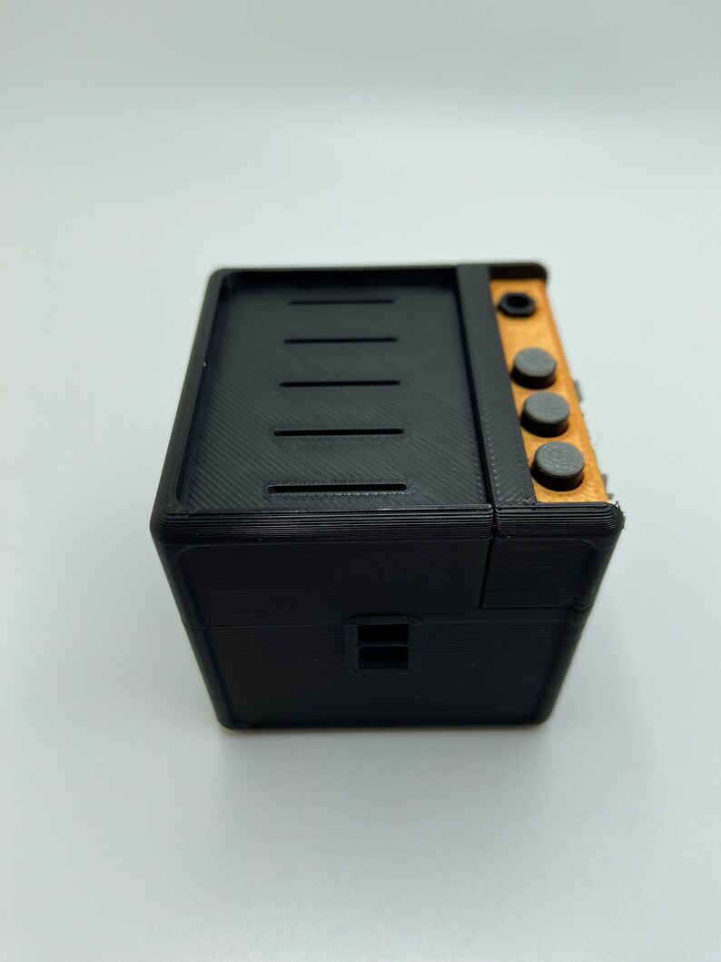 May include: A black and brown miniature stove with four black knobs and a small window. The stove is made of plastic and has a textured surface.