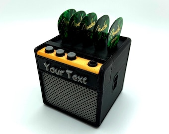 May include: A black and yellow miniature guitar amplifier with a speaker grill and four green guitar picks on top. The amplifier has a label that says "Your Text".
