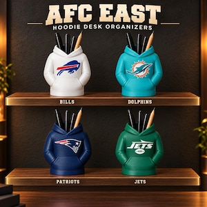 May include: Four hoodie-shaped desk organizers labeled AFC EAST HOODIE DESK ORGANIZERS. The white Bills, teal Dolphins, navy Patriots, and green Jets organizers each hold black pens and a pencil, featuring their respective team logos on the front.