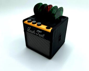 May include: A black and yellow miniature guitar amplifier with a speaker grill and four guitar picks on top. The amplifier has the text "Your Text" on the front.