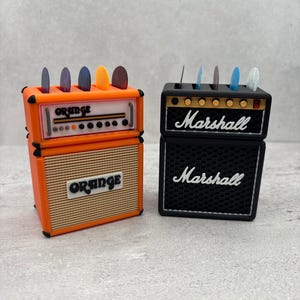 May include: Two miniature guitar amplifier models, one orange with "ORANGE" text and the other black with "Marshall" text. Both have slots holding guitar picks in various colors.