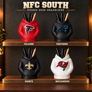 May include: Four hoodie-shaped desk organizers labeled NFC SOUTH HOODIE DESK ORGANIZERS. The red Falcons, black Panthers, black Saints, and white Buccaneers organizers each hold black pens and a pencil, featuring their respective team logos.