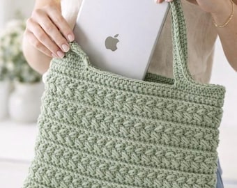 May include: A sage green crochet tote bag with a textured stitch pattern. The bag has two handles and is holding a silver tablet with the Apple logo. The bag is a handmade item.