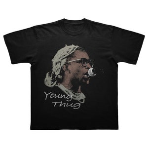 Puede incluir: Camiseta negra con una impresión blanca de un rapero con gafas y un micrófono. El texto "Young Thug" está impreso debajo de la imagen.