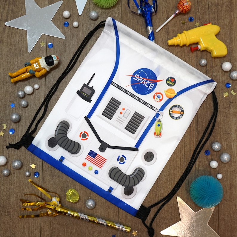 May include: A white drawstring backpack with a space theme. The backpack features a zipper, a NASA logo, and the word "SPACE" in blue letters. The backpack is decorated with various space-themed graphics, including a rocket, a planet, and stars.