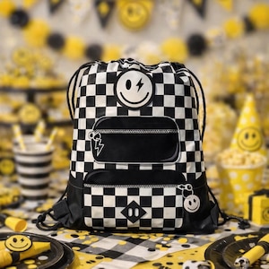 Puede incluir: Mochila con cordón a cuadros blancos y negros con un diseño de cara sonriente y rayo. La mochila tiene dos bolsillos con cremallera y un llavero de carita sonriente. El fondo presenta decoraciones de fiesta amarillas y negras.