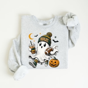 A gray sweatshirt with a graphic design depicting a ghost character wearing a football hat and holding a football, along with a pumpkin and a cup of coffee.