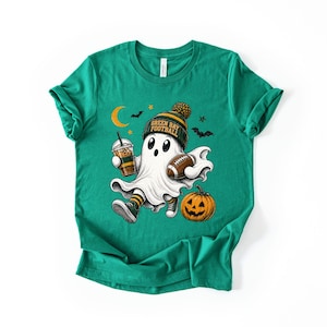 A green t-shirt with a graphic design featuring a ghost character holding a football and a pumpkin, along with Halloween-themed elements such as bats and a crescent moon.