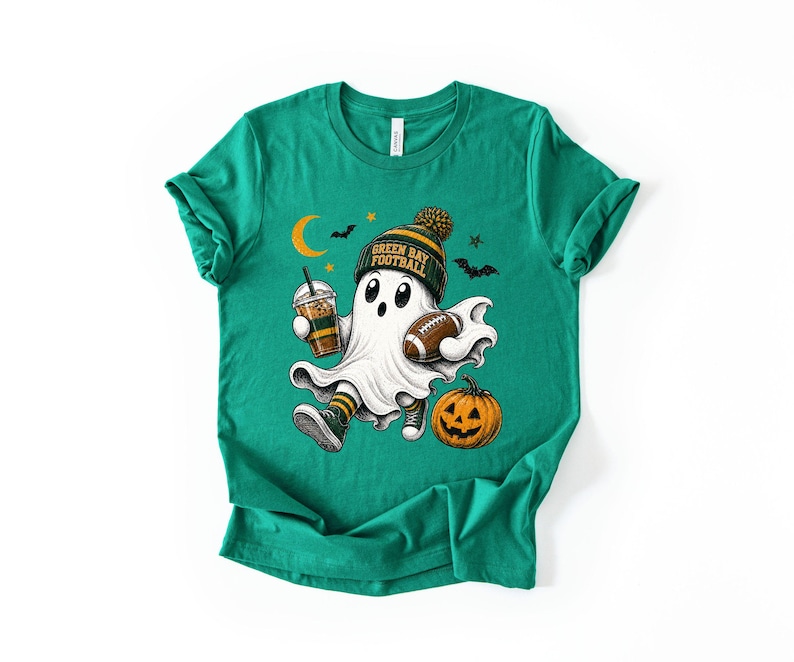 A green t-shirt with a graphic design featuring a ghost character holding a football and a pumpkin, along with Halloween-themed elements such as bats and a crescent moon.