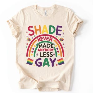 May include: A beige t-shirt with a rainbow graphic and the text "SHADE NEVER MADE ANYBODY LESS GAY."