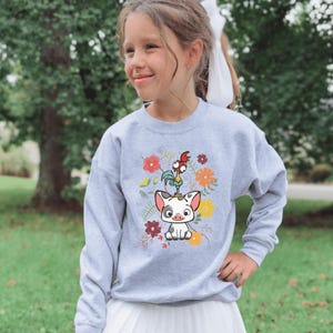 May include: A light gray sweatshirt featuring a colorful graphic of a pig, rooster, and flowers. The design includes red, orange, and yellow flowers. The sweatshirt is a crew neck style.