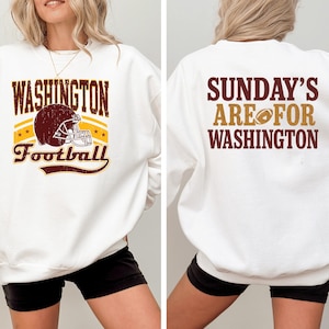 May include: White sweatshirt with the text "WASHINGTON Football" in maroon and gold, featuring a football helmet graphic. The back of the sweatshirt says "SUNDAY'S ARE FOR WASHINGTON" in maroon and gold.