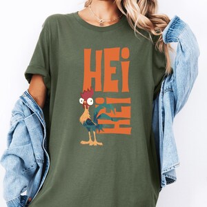 Op de afbeelding: Een groen T-shirt met een oranje afbeelding van een haan en het woord "Hei" dat verticaal wordt herhaald.