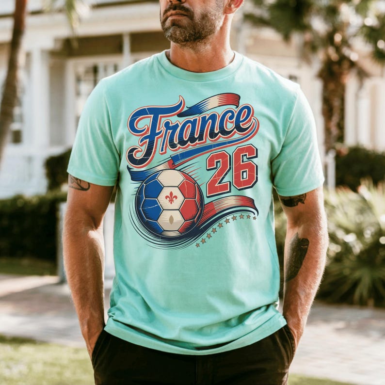 K&ouml;nnte beinhalten: Hellblaues T-Shirt mit dem Wort "France" in Schreibschrift, einem Fu&szlig;ball und der Zahl "26". Der Fu&szlig;ball hat die Farben der franz&ouml;sischen Flagge. Das Shirt hat einen Vintage-Look.