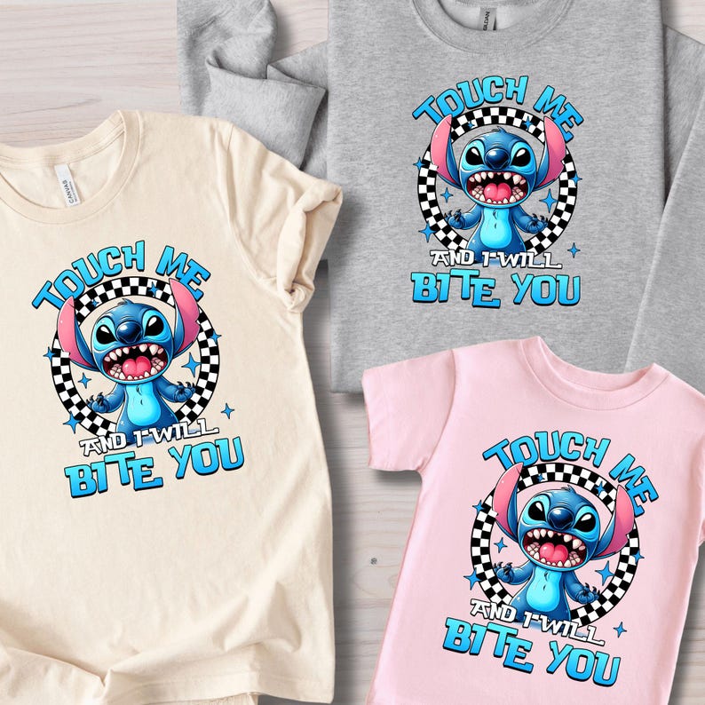 May include: A collection of t-shirts and a sweatshirt featuring a cartoon character. Each shirt displays the text "TOUCH ME AND I WILL BITE YOU" with a blue alien character in a black and white checkered circle. The shirts are in beige, gray, and pink.