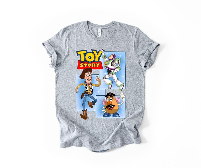 May include: A heather gray short-sleeve t-shirt featuring a graphic print of the Toy Story logo and characters Woody, Buzz Lightyear, and Mr. Potato Head. The design is set against a light blue background with white star accents on the front.