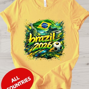 A yellow t-shirt with a graphic design featuring the text "brazil 2026" and a soccer ball, surrounded by splashes of green, yellow, and blue colors.