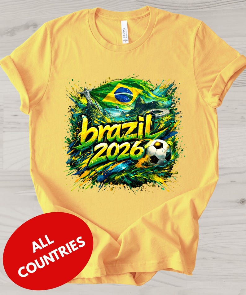 A yellow t-shirt with a graphic design featuring the text "brazil 2026" and a soccer ball, surrounded by splashes of green, yellow, and blue colors.