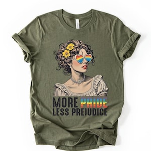 May include: Olive green t-shirt featuring a graphic of a woman wearing heart-shaped rainbow sunglasses and yellow flowers in her hair. The text "MORE PRIDE LESS PREJUDICE" is printed below the graphic in rainbow colors.