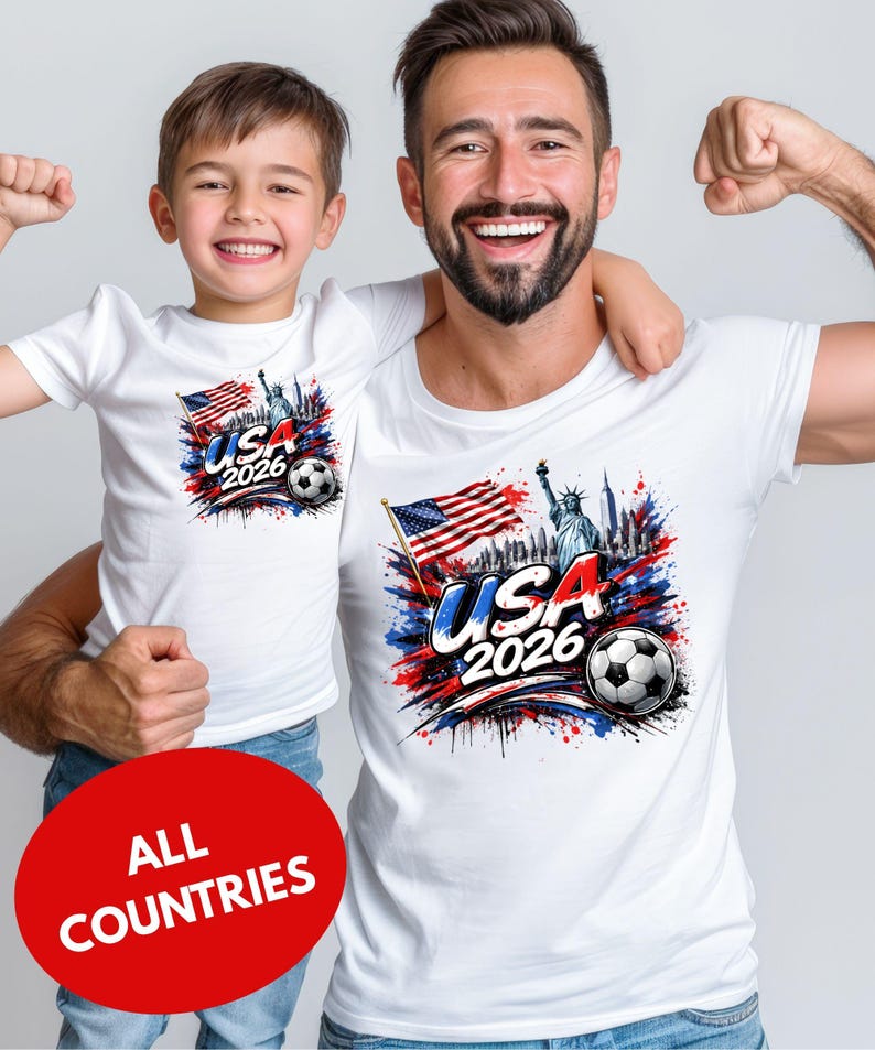 A man and a young boy wearing matching white t-shirts with a graphic design featuring the text "USA 2026" and an American flag, along with a soccer ball.