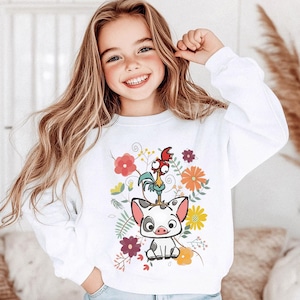 May include: White sweatshirt featuring a colorful graphic of a pig, a rooster, and floral elements. The design includes red, orange, and purple flowers. The sweatshirt is worn by a young girl with long blonde hair.
