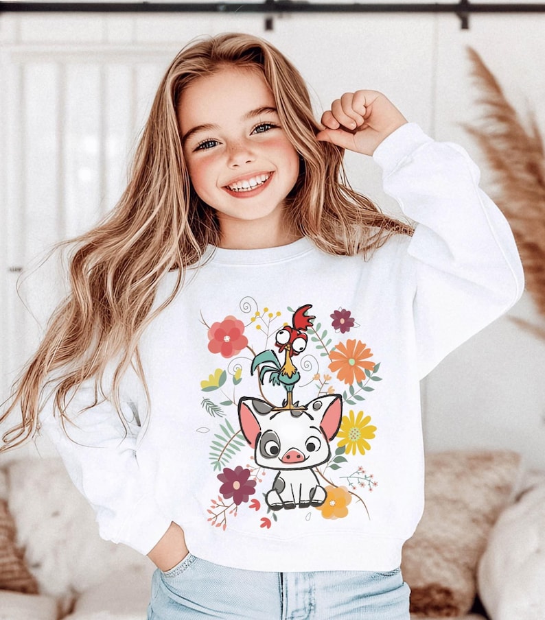 May include: White sweatshirt featuring a colorful graphic of a pig, a rooster, and floral elements. The design includes red, orange, and purple flowers. The sweatshirt is worn by a young girl with long blonde hair.