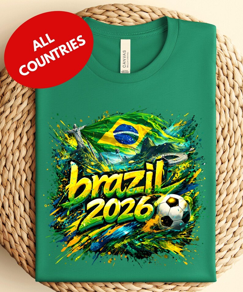 A green t-shirt with a vibrant graphic design featuring the text "brazil 2026" and a soccer ball, surrounded by splashes of color and the Brazilian flag.