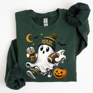 A green sweatshirt with a Halloween-themed graphic design featuring a ghost character holding a football and a pumpkin.