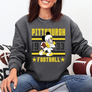 May include: Dark gray sweatshirt featuring a graphic of Mickey Mouse in a football uniform. The design includes the text "PITTSBURGH 1933 FOOTBALL" in yellow and black. A football is visible.