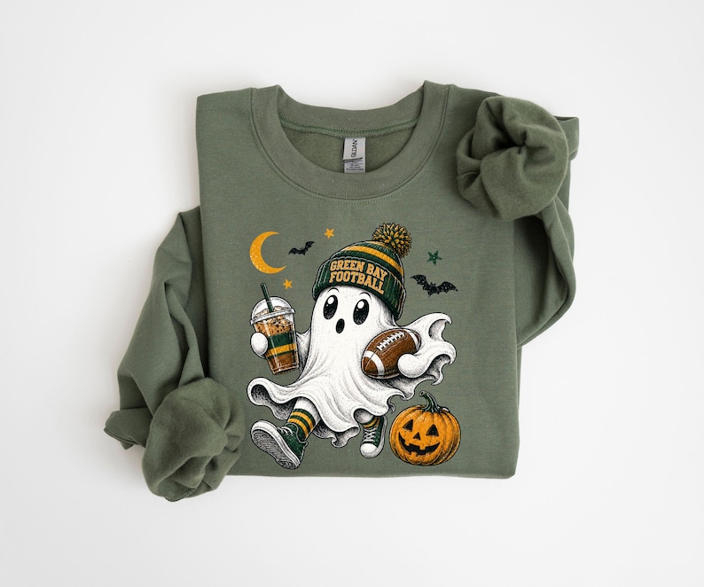 A green sweatshirt with a graphic design depicting a ghost character holding a football and a pumpkin, along with Halloween-themed elements such as bats and a crescent moon.