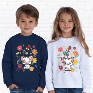May include: Two children wearing sweatshirts. One is navy blue, the other is white. Both sweatshirts feature a cartoon pig with a rooster on its head, surrounded by colorful flowers. The design is a whimsical illustration.