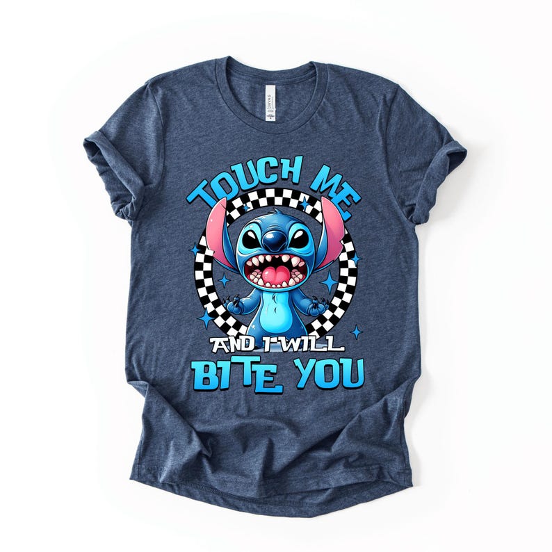 May include: A navy blue t-shirt featuring a cartoon character with blue fur, large ears, and a wide grin. The text "TOUCH ME AND I WILL BITE YOU" is printed in blue, with the character in the center of a black and white checkered circle.