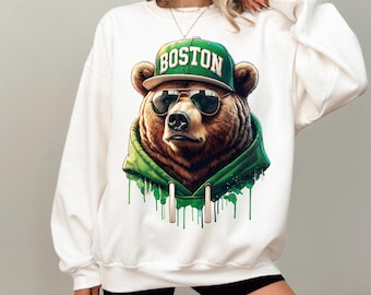 May include: White sweatshirt with a graphic print of a brown bear wearing sunglasses and a green baseball cap that says "BOSTON".