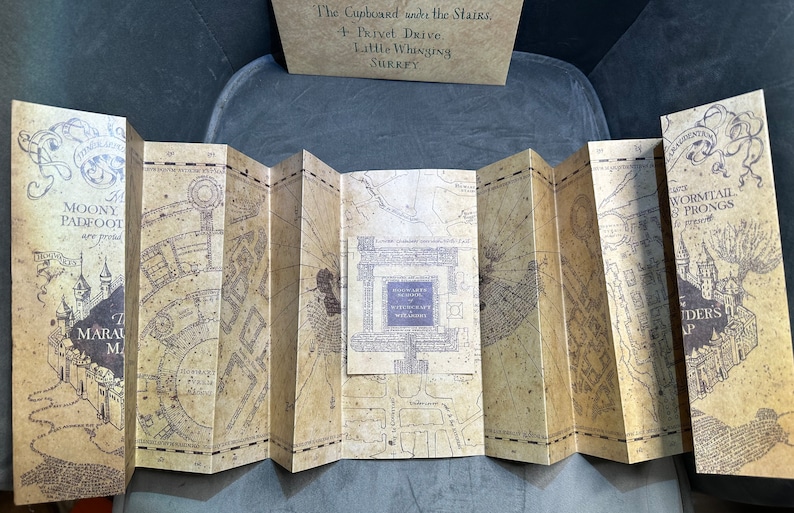 K&ouml;nnte beinhalten: Eine braune und beigefarbene Papierkarte mit einer detaillierten Illustration einer Stadt. Die Karte ist in Abschnitte gefaltet und tr&auml;gt den Text "Marauder's Map" und "Moony Padfoot Wormtail Prongs".