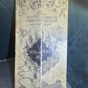 K&ouml;nnte beinhalten: Eine Karte im Vintage-Stil von Hogwarts, der fiktiven Schule aus der Harry-Potter-Reihe. Die Karte tr&auml;gt den Titel "Die Karte der Marauder" und enth&auml;lt den Text "Moony, Wormtail, Padfoot, Prongs pr&auml;sentieren mit Stolz."