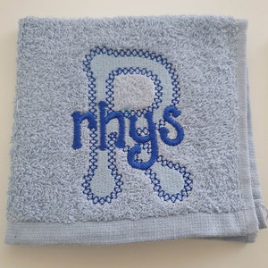 May include: A light blue towel with a blue embroidered letter R and the name Rhys in blue embroidery.